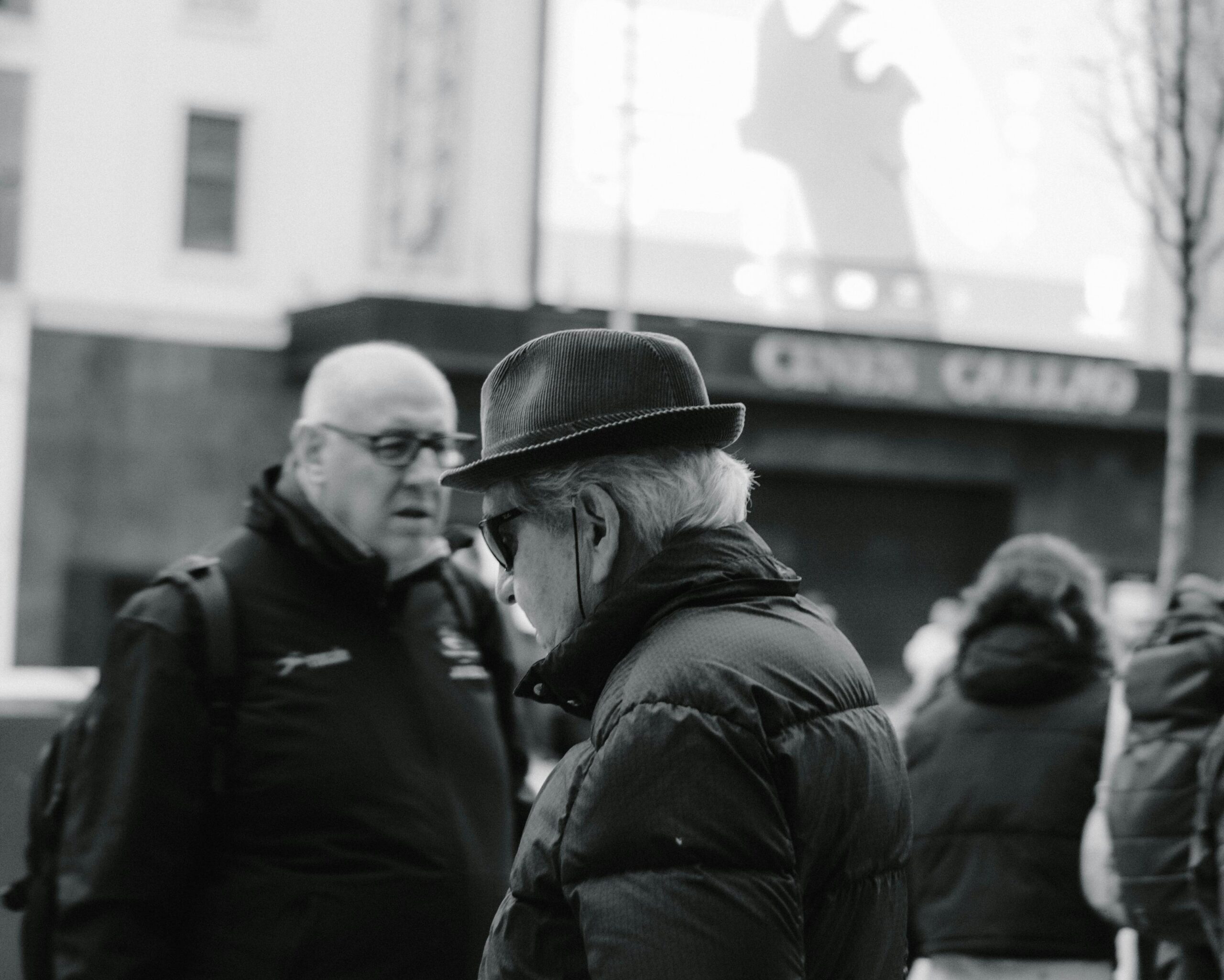 Two elderly men conversing in an urban setting captured in black and white, highlighting city life.